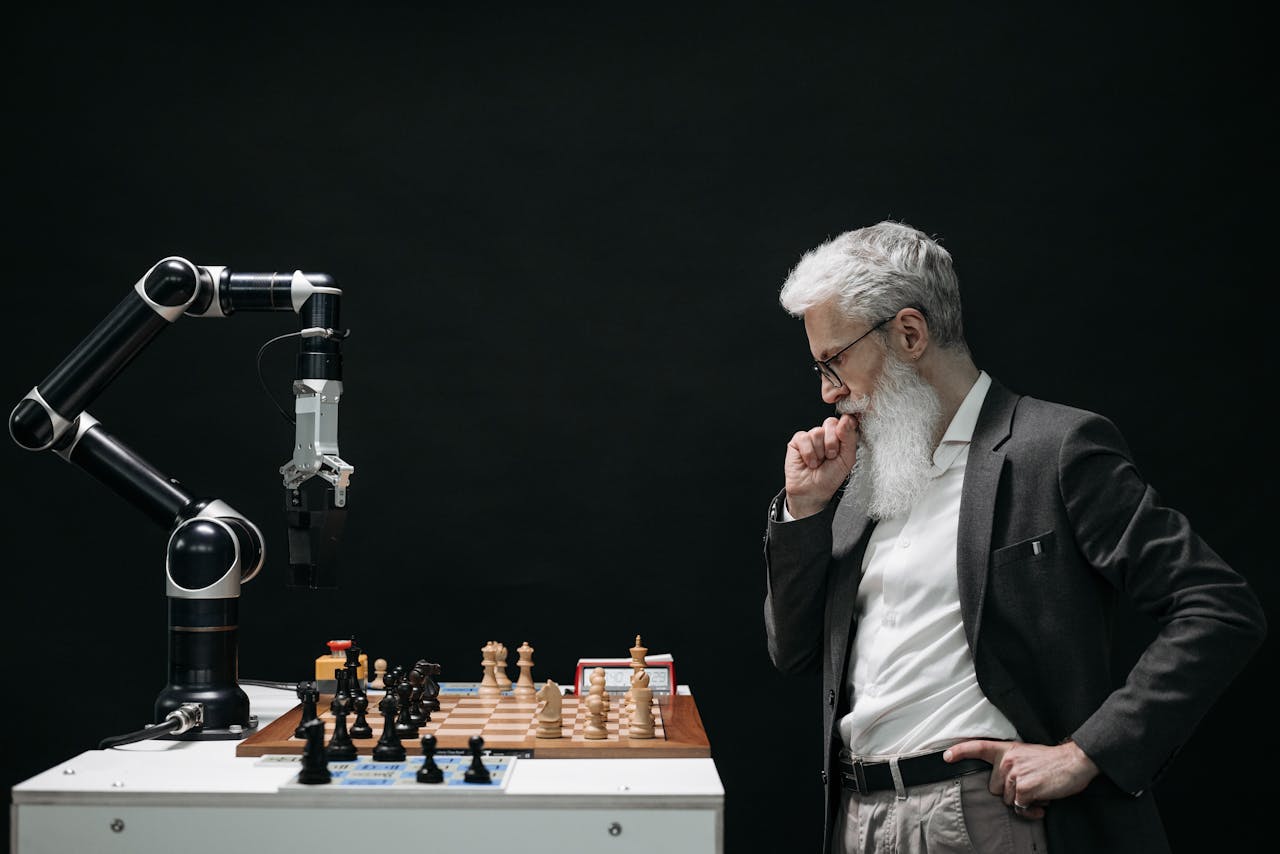 services-03 An elderly scientist contemplates a chess move against a robotic arm on a chessboard.